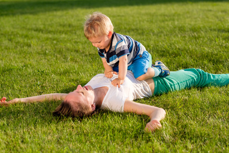 Happy woman and child having fun outdoor on meadow.  Family lifestyle scene of mother and son resting together on green grass in the park.の写真素材