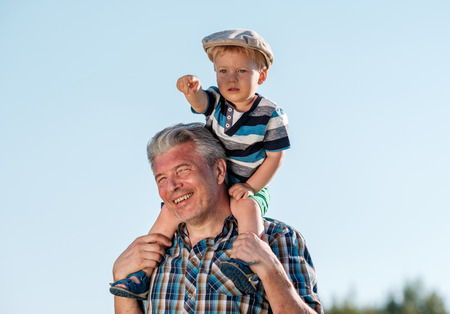 Grandfather carries grandson toddler boy on his shoulders. Child having piggyback ride on his...