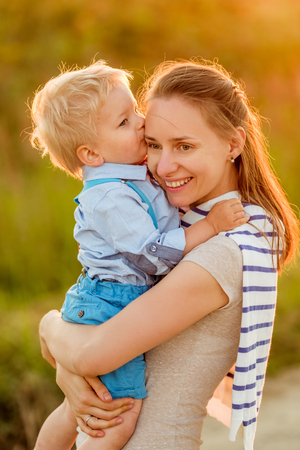 Happy woman and child having fun outdoors.  Family lifestyle rural scene of mother and son in sunset sunlight. Boy kissing his mom.の写真素材