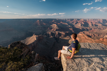 Tourist with backpack at Grand Canyon sitting on the rock edge, Arizona, USAの写真素材