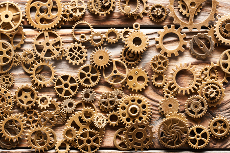 Various metal cogwheels and gear wheels over wooden background