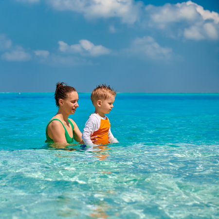 Three year old toddler boy on beach with mother having fun in shallow water. Summer family vacation at Maldives.の写真素材