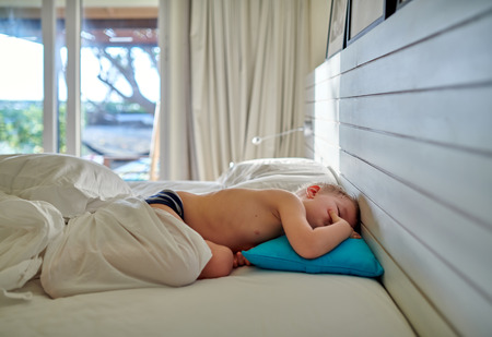 Three year old toddler boy sleeping on blue pillow under blanketの写真素材