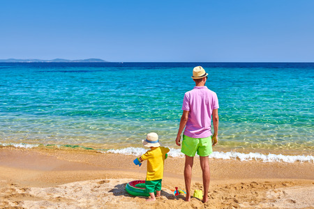 Two year old toddler boy on beach with father. Inflatable ring and beach toys. Summer family vacation. Sithonia, Greece.の写真素材