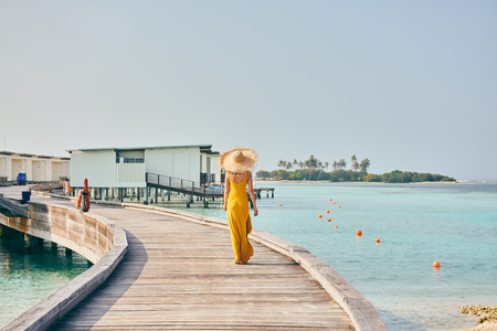 Woman in dress walking on tropical beach boardwalk. Summer vacation at Maldives.の写真素材