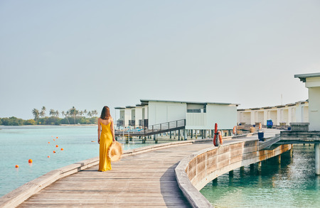 Woman in dress walking on tropical beach boardwalk. Summer vacation at Maldives.の写真素材