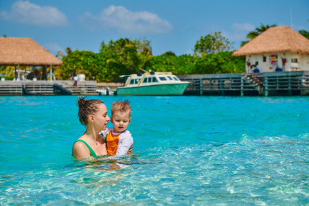 Three year old toddler boy on beach with mother having fun in shallow water. Summer family vacation at Maldives.の写真素材