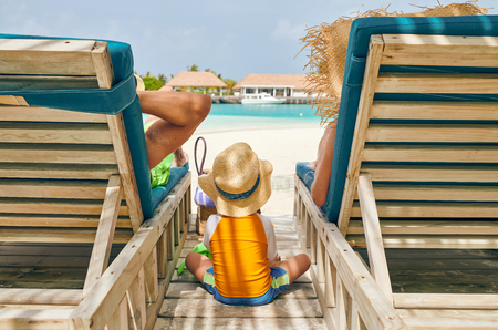 Family at beach on wooden sun bed loungers, young couple with three year old boy. Summer vacation at Maldives.の写真素材