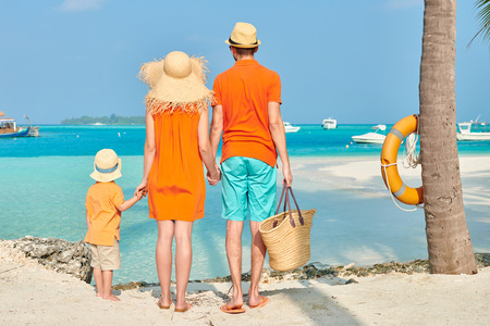 Family on beach, young couple in orange with three year old boy under the palm tree. Summer vacation at Maldives.の写真素材