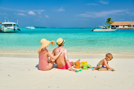 Family on beach, young couple with three year old boy. Woman applying sun screen protection lotion on man's back. Summer vacation at Maldives.の写真素材