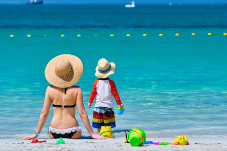 Two year old toddler boy playing with beach toys with mother on beachの写真素材