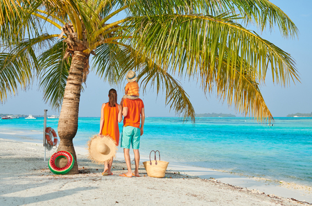 Family on beach, young couple in orange with three year old boy under the palm tree. Summer vacation at Maldives.の写真素材