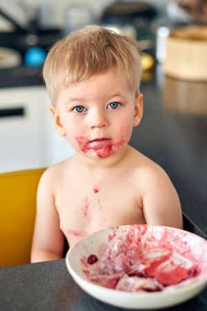 Adorable two years old boy playing with food. Toddler child eating fruit. Dirty messy face of happy kid.の写真素材