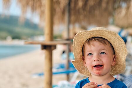 Two year old toddler boy on beach eating fruit. Dirty messy face of happy kid.の写真素材