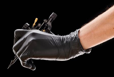Tattoo machine in artist's hand isolated on black backgroundの写真素材