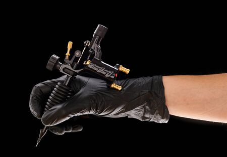 Tattoo machine in artist's hand isolated on black backgroundの写真素材