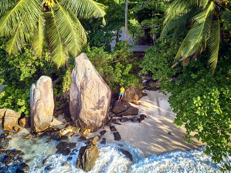 Man on beautiful beach with palm tree and rocks aerial top view drone shot at Seychelles, Maheの写真素材