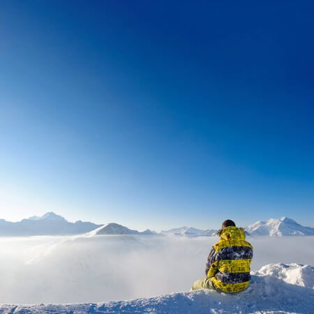 Alpine winter mountain landscape with man sitting above low clouds. French Alps covered with snow in sunny day. Val-d'Isere, Franceの写真素材