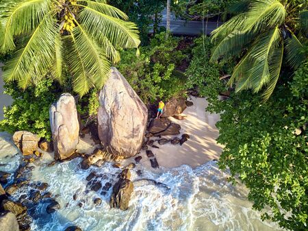Man on beautiful beach with palm tree and rocks aerial top view drone shot at Seychelles, Maheの写真素材