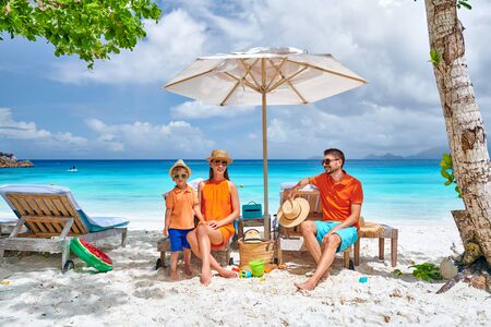 Family on beautiful Petite Anse beach, young couple with three year old toddler boy sitting on sun bed. Summer vacation at Seychelles, Mahe.の写真素材