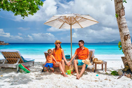 Family on beautiful Petite Anse beach, young couple with three year old toddler boy sitting on sun bed.の写真素材