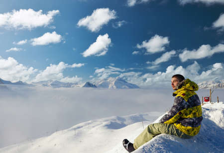 Alpine winter mountain landscape with man sitting above low clouds. French Alps covered with snow in sunny day. Val-d'Isere, Franceの写真素材