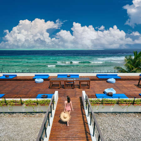 Woman in red striped one-piece swimsuit walking on tropical beach patio deck. Summer vacation at Maldives.の写真素材