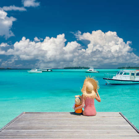 Three year old toddler boy with mother sitting on wooden jetty. Summer family vacation at Maldives.の写真素材