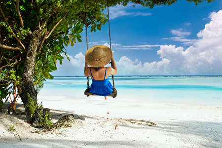 Woman in blue dress swinging at tropical beachの写真素材