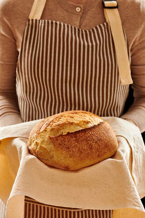 Baker woman holding rustic organic loaf of tartine homemade bread in hands
