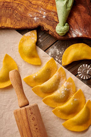 Tasty raw homemade ravioli pasta with spinach and ricotta on wooden rustic background. Process of making Italian ravioli.の写真素材