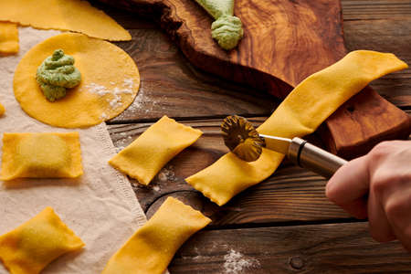 Tasty raw homemade ravioli pasta with spinach and ricotta on wooden rustic background. Process of making Italian ravioli.の写真素材