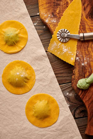 Tasty raw homemade ravioli pasta with spinach and ricotta on wooden rustic background. Process of making Italian ravioli.の写真素材
