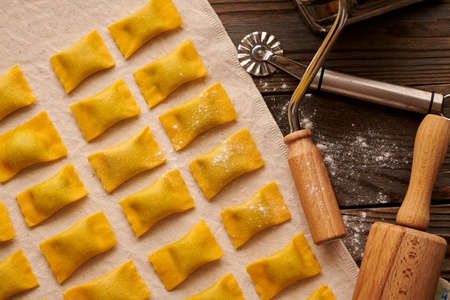 Tasty raw homemade ravioli pasta with spinach and ricotta on wooden rustic background. Process of making Italian ravioli.の写真素材