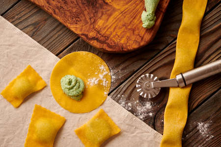 Tasty raw homemade ravioli pasta with spinach and ricotta on wooden rustic background. Process of making Italian ravioli.の写真素材