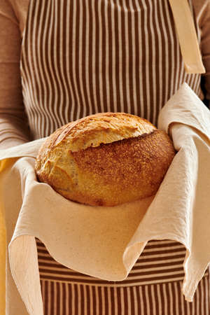 Baker woman holding rustic organic loaf of tartine homemade bread in handsの写真素材