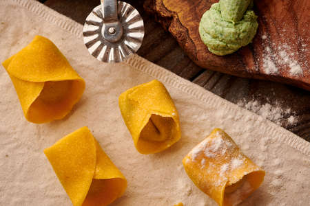 Tasty raw homemade ravioli pasta with spinach and ricotta on wooden rustic background. Process of making Italian ravioli.の写真素材