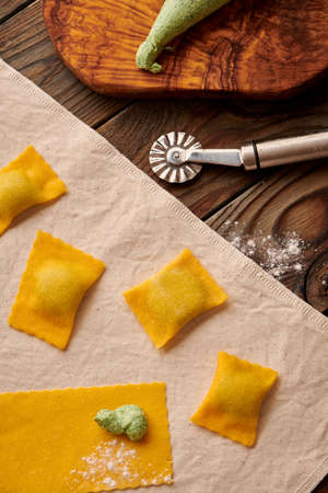 Tasty raw homemade ravioli pasta with spinach and ricotta on wooden rustic background. Process of making Italian ravioli.の写真素材