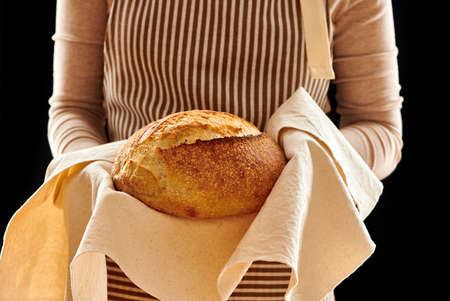 Baker woman holding rustic organic loaf of tartine homemade bread in handsの写真素材