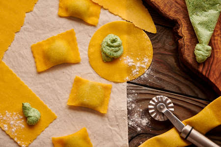 Tasty raw homemade ravioli pasta with spinach and ricotta on wooden rustic background. Process of making Italian ravioli.の写真素材