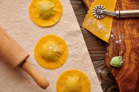 Tasty raw homemade ravioli pasta with spinach and ricotta on wooden rustic background. Process of making Italian ravioli.の写真素材