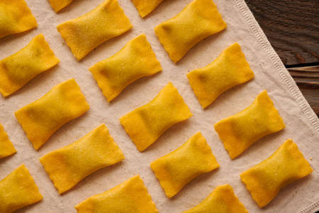 Tasty raw homemade ravioli pasta with spinach and ricotta on wooden rustic background. Process of making Italian ravioli.の写真素材