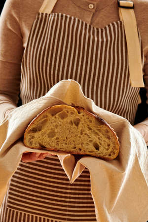 Baker woman holding rustic organic loaf of tartine homemade bread in handsの写真素材