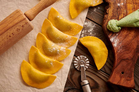 Tasty raw homemade ravioli pasta with spinach and ricotta on wooden rustic background. Process of making Italian ravioli.の写真素材