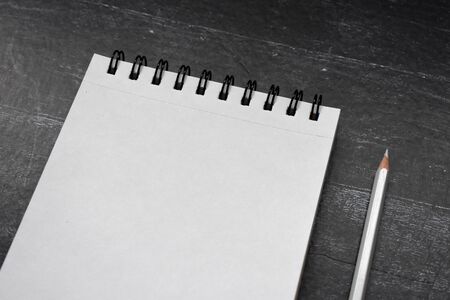 Clear sheet note book and white pencil on black wood background.