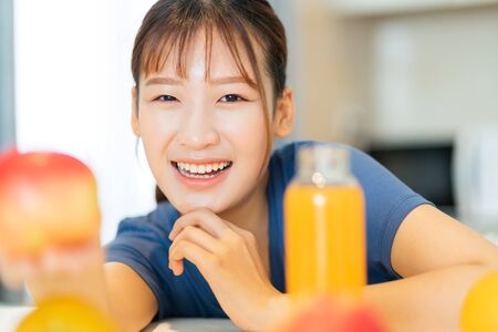 A young Asian woman eating breakfast with fruit in her kitchenの写真素材