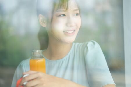 Young Asian woman drink orange juice beside the window at morningの写真素材