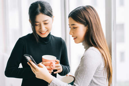 Two asian business women were chatting by the window during recess.