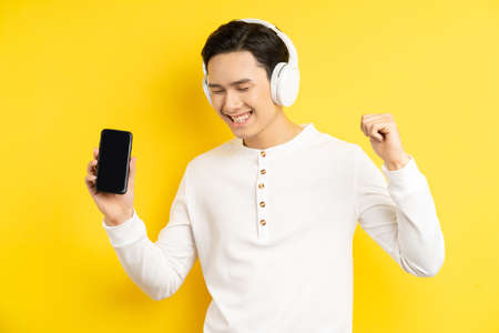Asian businessman is listening to music with wireless headphones, holding a ming smartphone in his...