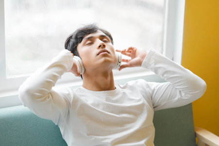 Asian man sitting, enjoying musicの写真素材